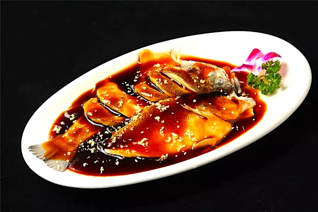 Whole grass carp poached and glazed with sweet vinegar, served on white platter with orchid garnish