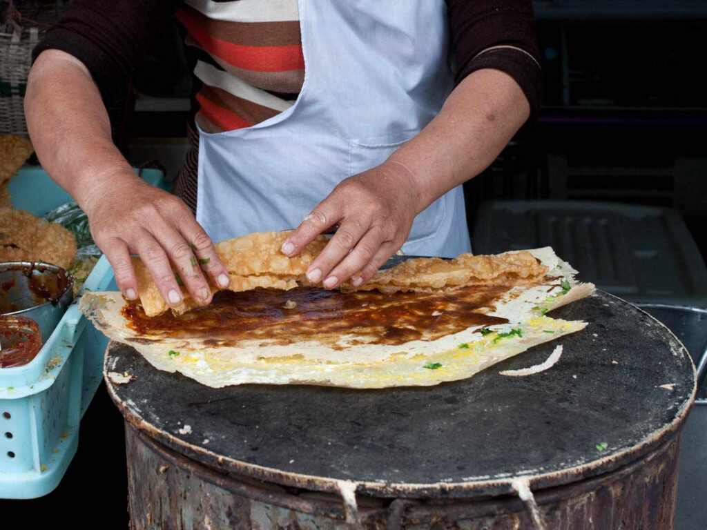 Street vendor making jianbing on griddle with youtiao