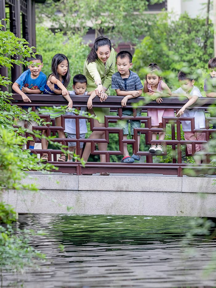 Children and teacher on a wooden bridge over water in a Chinese garden